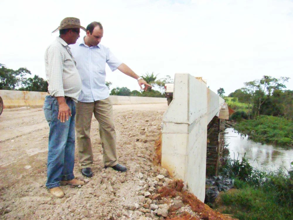Ari Saraiva apontando para a cabeceira de uma ponte de concreto sobre o rio.